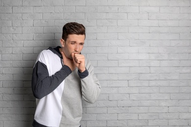 Photo of Young man coughing on brick wall background