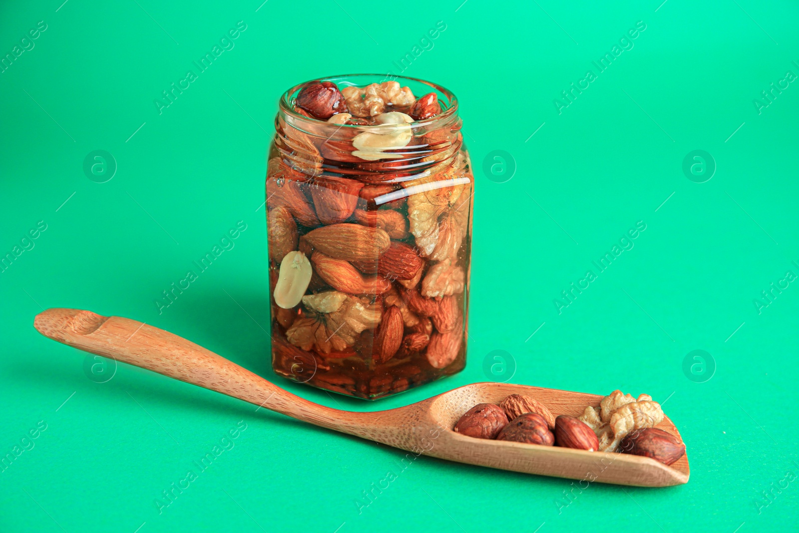 Photo of Different tasty nuts with honey on green background