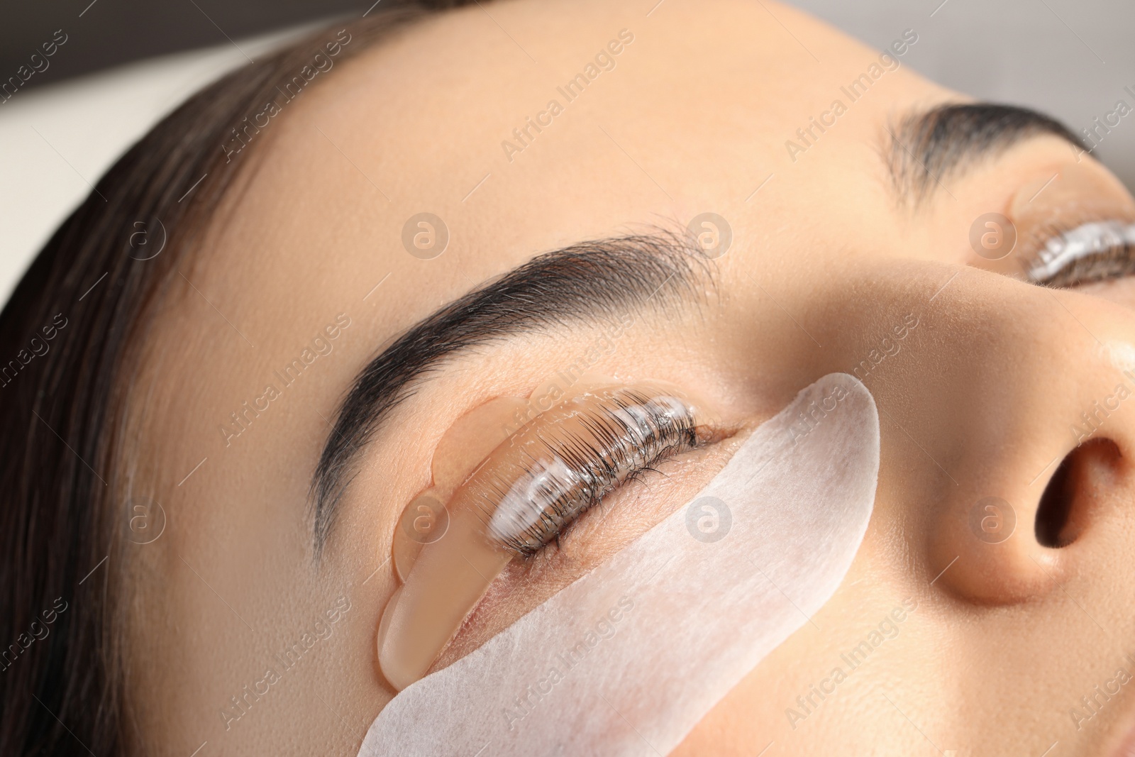 Photo of Young woman undergoing eyelash lamination, closeup. Professional service