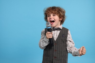Photo of Cute little boy with microphone singing on light blue background, space for text