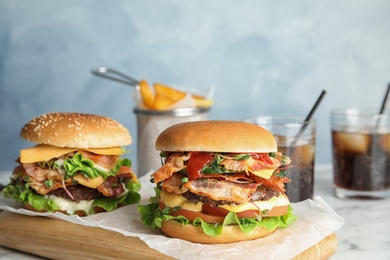 Tasty burgers with bacon on board against color background