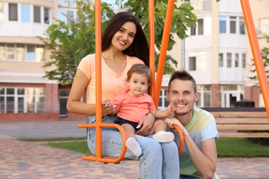 Photo of Happy family with adorable little baby at playground