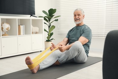 Photo of Senior man doing exercise with fitness elastic band on mat at home