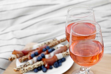 Photo of Glasses of delicious rose wine and food on white picnic blanket, closeup