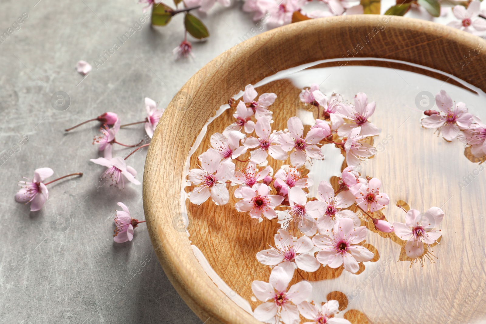 Photo of Bowl with water and blossoming flowers on grey background