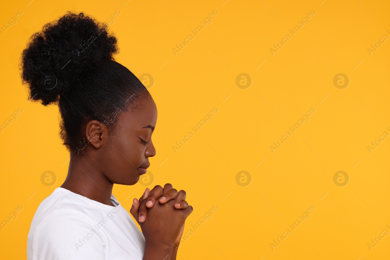 Photo of Woman with clasped hands praying to God on orange background. Space for text