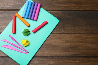 Photo of Many different colorful plasticine pieces with tools on wooden table, top view. Space for text