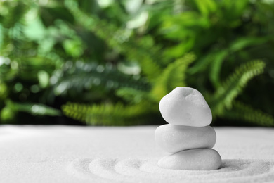 Stack of white stones on sand against blurred green background, space for text. Zen, meditation, harmony