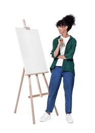 Photo of Young woman holding brush near easel with canvas against white background