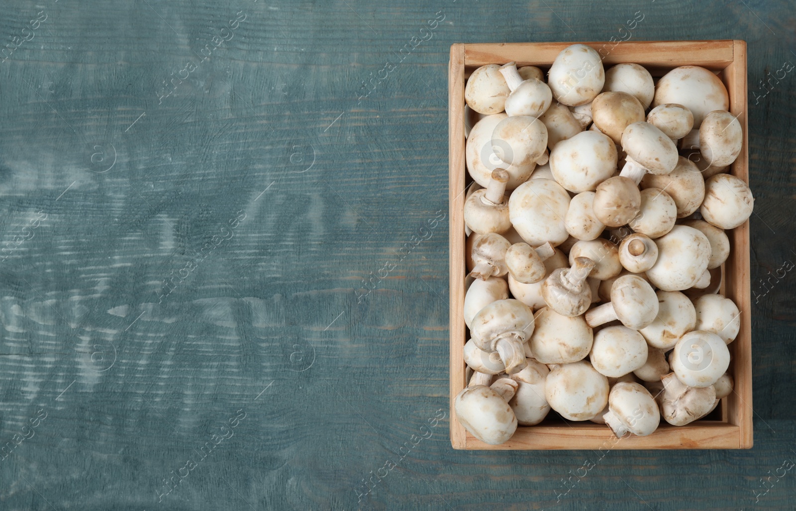 Photo of Wooden crate full of fresh raw mushrooms on table, top view. Space for text