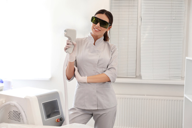 Photo of Young woman holding professional laser epilator in beauty salon