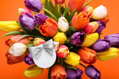 Photo of Bouquet of beautiful colorful tulips with blank card on orange background, above view. Birthday celebration
