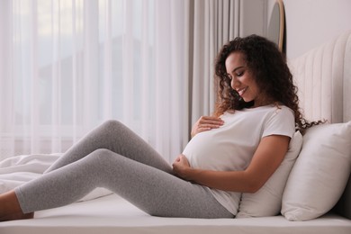 Photo of Pregnant young African-American woman sitting on bed at home