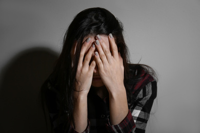Abused young woman crying near beige wall. Domestic violence concept