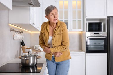 Photo of Menopause. Woman suffering from abdominal pain near cooktop in kitchen, space for text