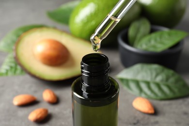 Photo of Dripping avocado essential oil into bottle on table, closeup