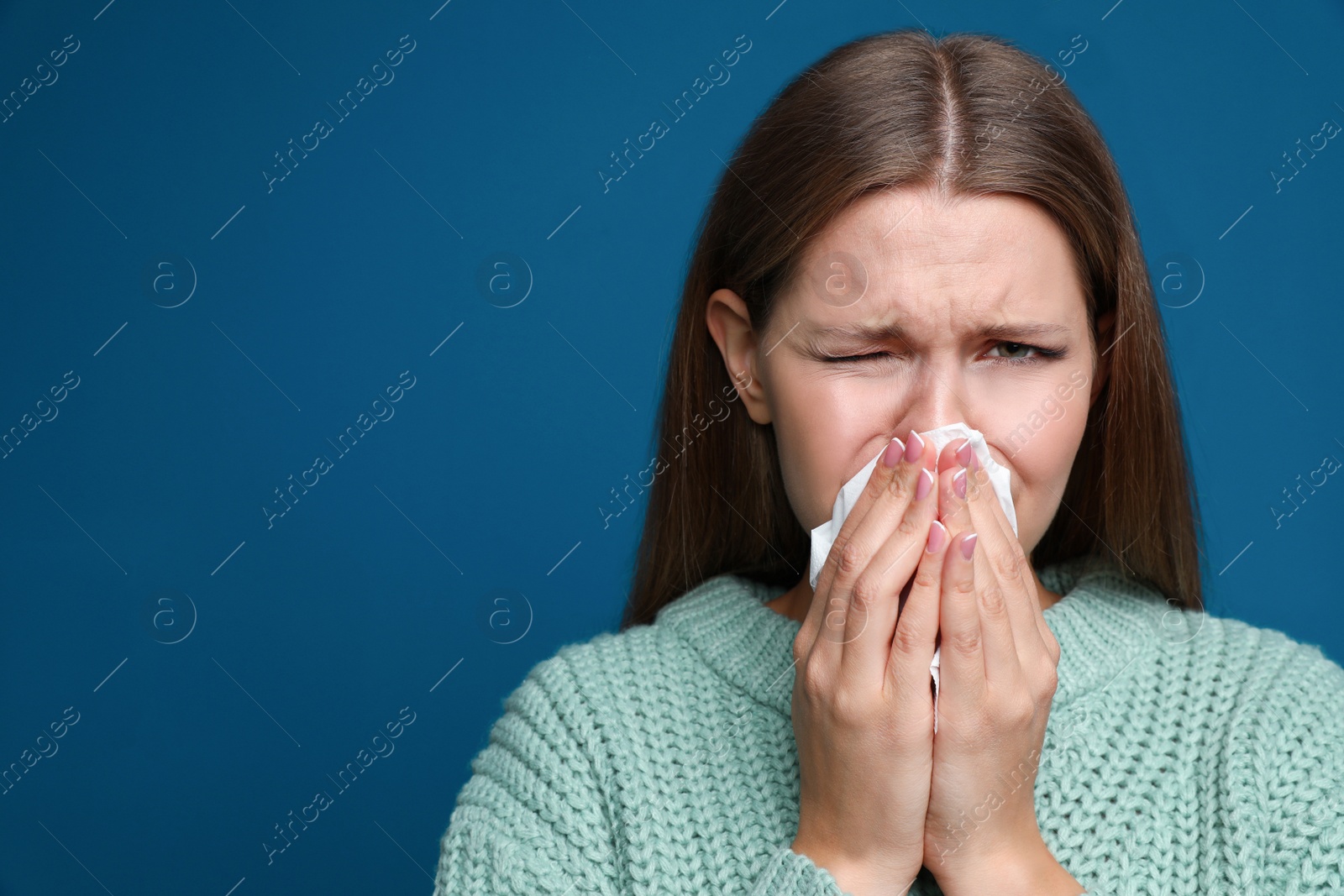 Image of Young woman sneezing on blue background, space for text. Cold symptoms