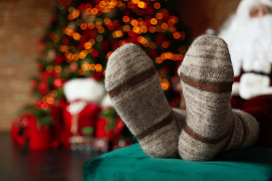 Photo of Santa Claus wearing woolen socks against blurred Christmas lights, closeup