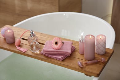 Photo of Wooden bath tray with candles and personal care products on tub indoors