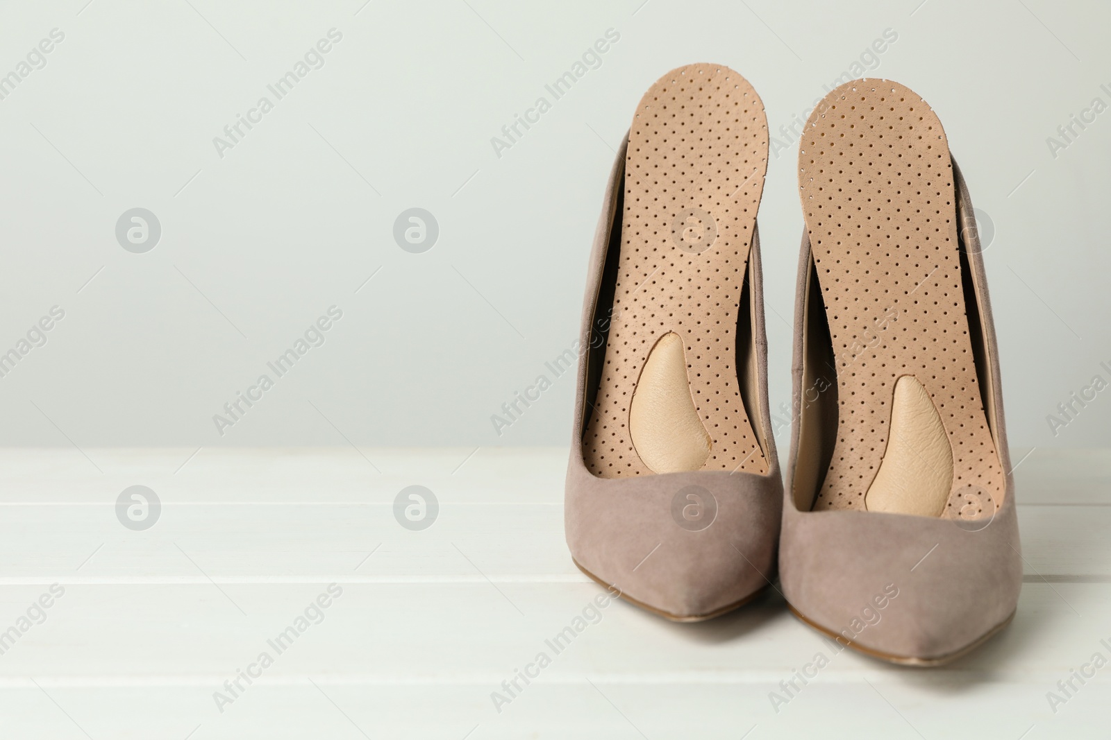 Photo of Orthopedic insoles in high heel shoes on white wooden floor, closeup. Space for text