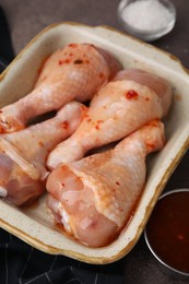 Fresh marinade and raw chicken drumsticks on brown table, closeup