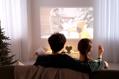 Photo of Couple watching romantic Christmas movie via video projector at home, back view