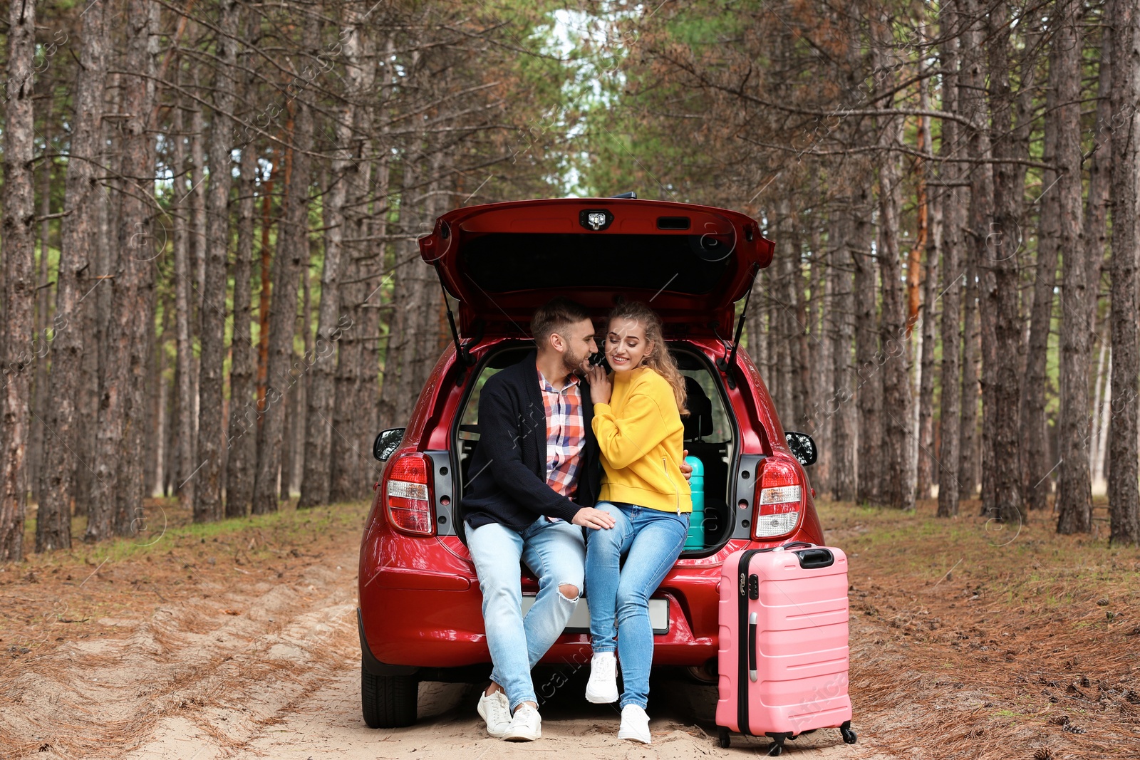 Photo of Young couple sitting in car trunk and suitcase on forest road