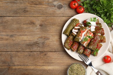 Photo of Delicious stuffed grape leaves with sour cream and tomato sauce on wooden table, flat lay. Space for text