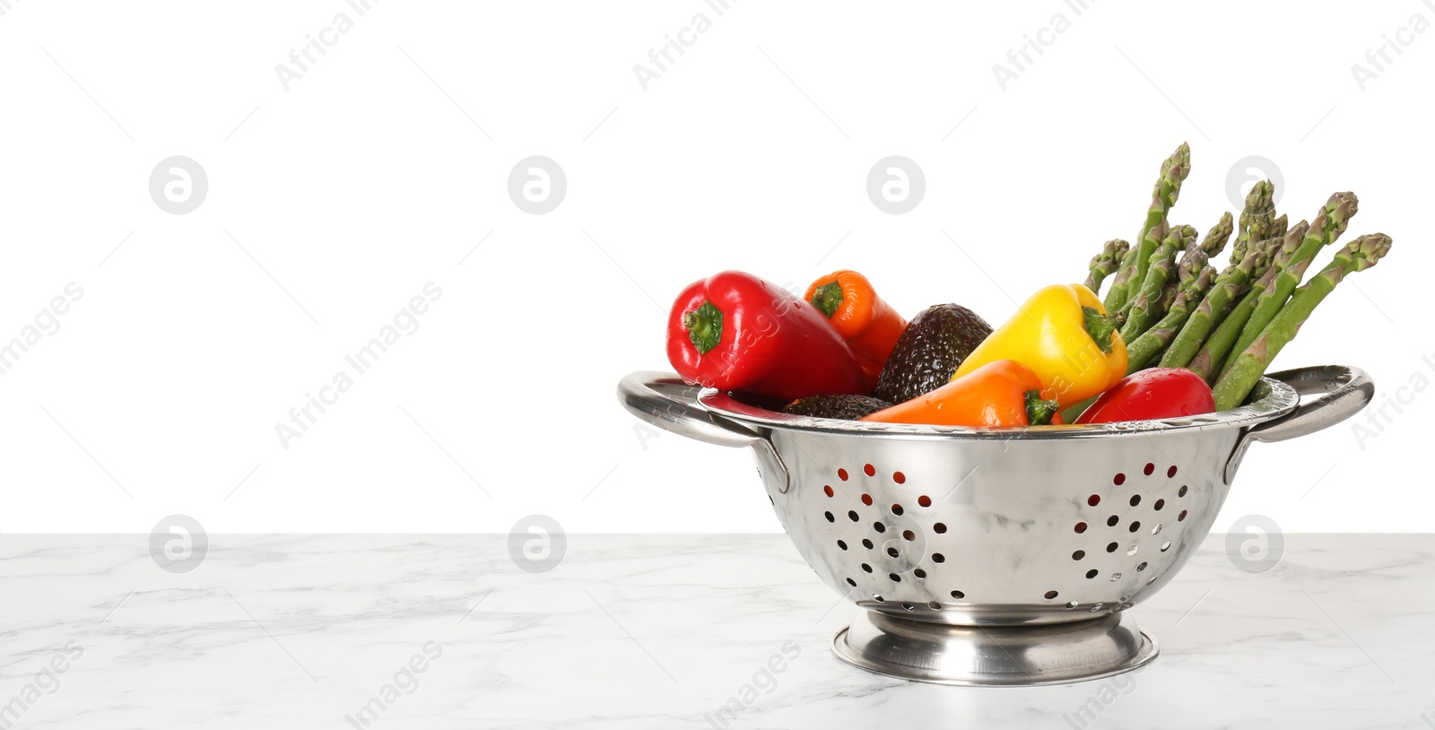 Photo of Metal colander with different vegetables and avocados on light marble table against white background, space for text