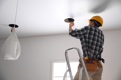 Photo of Worker installing lamp on stretch ceiling indoors. Space for text