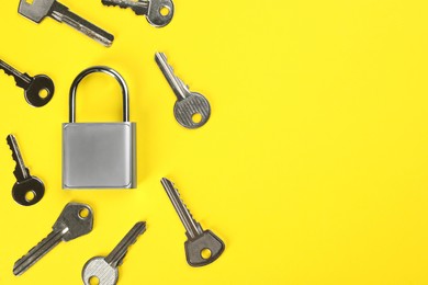 Photo of Modern padlock with keys on yellow background, flat lay. Space for text