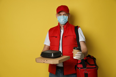 Courier in protective gloves and mask holding order on yellow background. Food delivery service during coronavirus quarantine