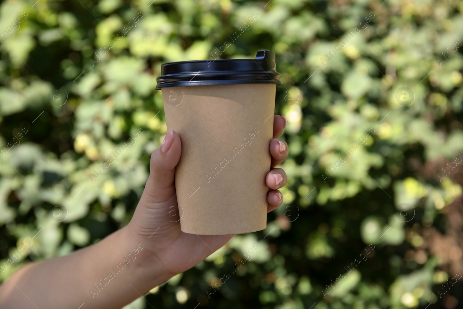 Photo of Woman holding takeaway cardboard coffee cup with plastic lid outdoors, closeup