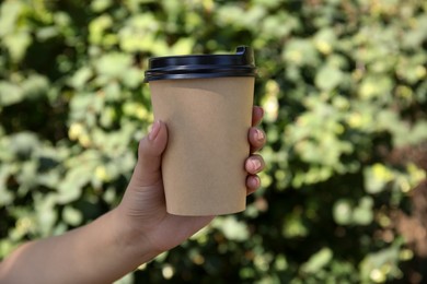 Woman holding takeaway cardboard coffee cup with plastic lid outdoors, closeup