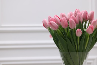 Bouquet of beautiful pink tulips near white wall, space for text