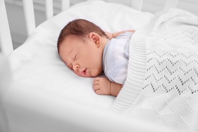 Cute newborn baby sleeping under plaid in crib