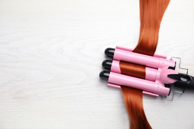 Curling iron with red hair lock on white wooden table, flat lay. Space for text