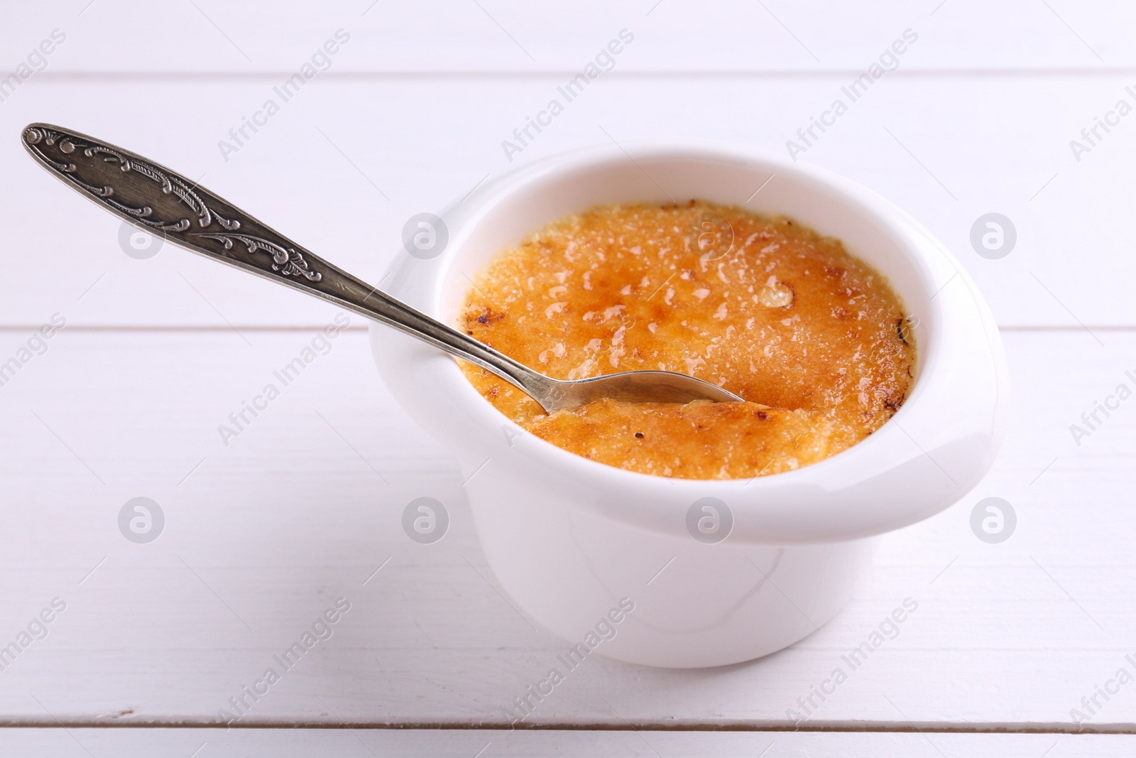 Photo of Delicious creme brulee in bowl served on white wooden table, closeup