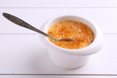 Photo of Delicious creme brulee in bowl served on white wooden table, closeup