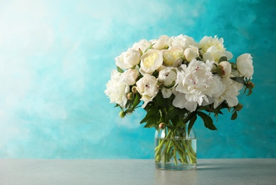 Photo of Fragrant peonies in vase on table against color background, space for text. Beautiful spring flowers