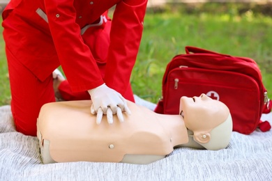 Photo of Woman in uniform practicing CPR on mannequin at first aid class outdoors