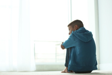 Photo of Upset boy sitting near window indoors. Space for text