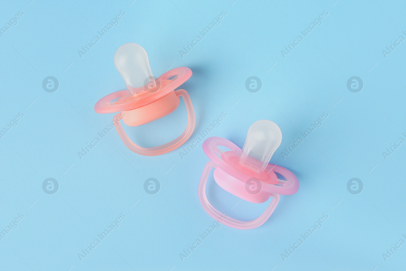 Photo of New baby pacifiers on light blue background, flat lay