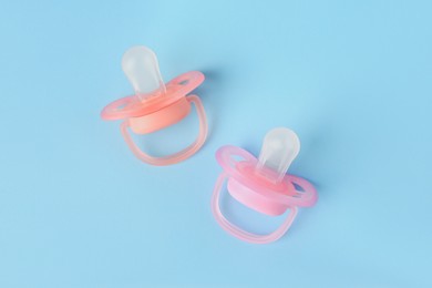 Photo of New baby pacifiers on light blue background, flat lay