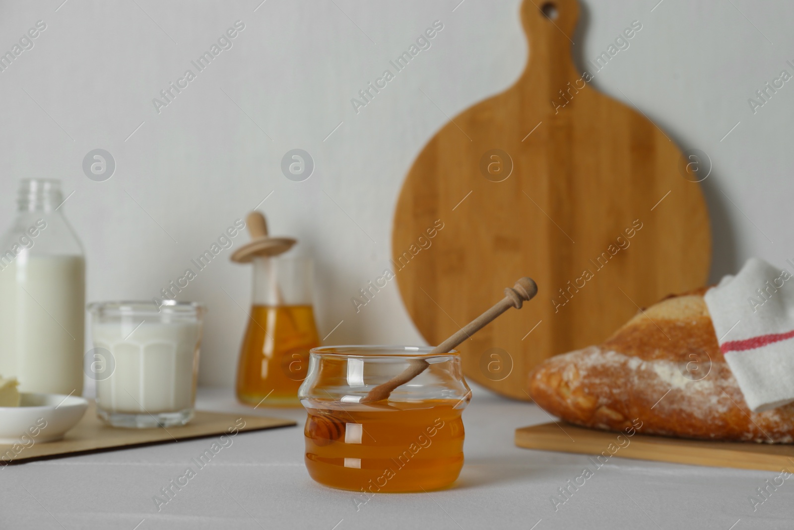 Photo of Jar with honey, milk, butter and bread served for breakfast on table indoors