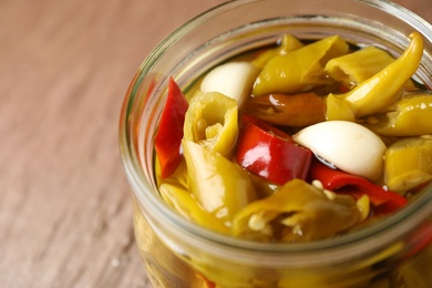 Photo of Glass jar with pickled peppers on brown table, closeup