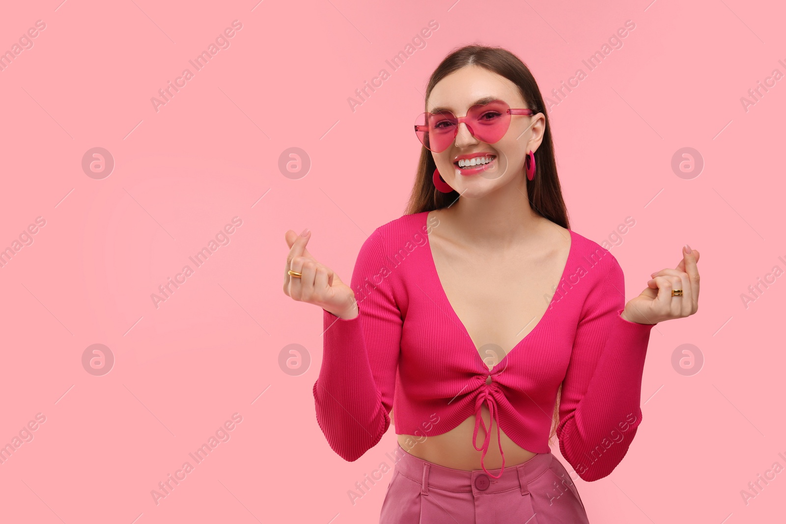 Photo of Beautiful woman in pink clothes showing finger heart gesture on color background, space for text