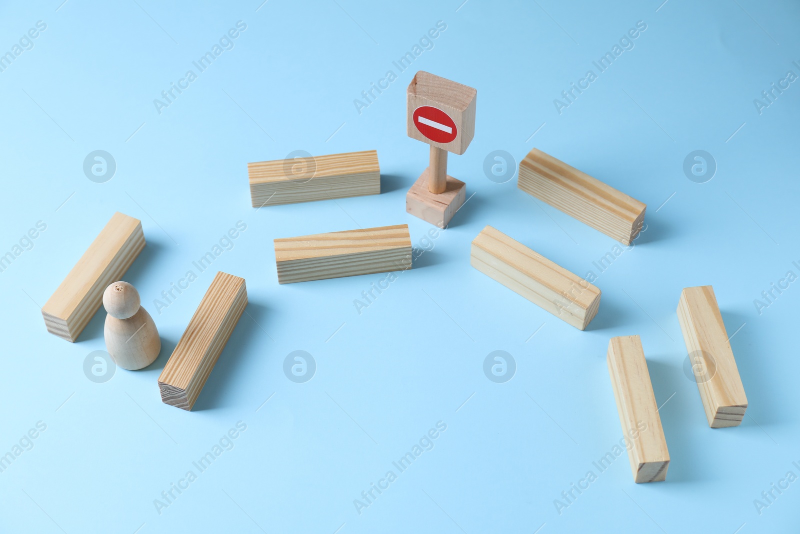 Photo of Overcoming barries for development and success. Wooden human figure movement blocked by road Stop sign on light blue background