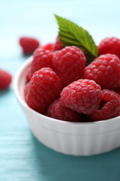 Photo of Delicious ripe raspberries in bowl on light blue wooden table, closeup