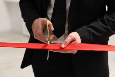 Photo of Man cutting red ribbon with scissors on blurred background, closeup